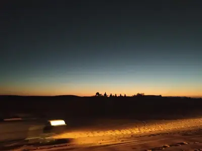 a car driving down a road at sunset at Afraklie Camp in Merzouga
