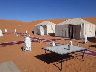 a picnic table in front of tents in the desert at Afraklie Camp in Merzouga