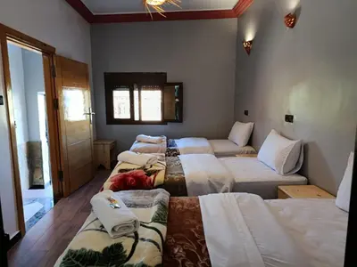 a room with four beds with white sheets and a window at Auberge Restaurant Camping Taghzout in Agoudal