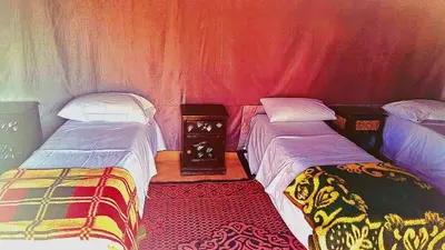 two twin beds in a room with red curtains at Tigmi Desert Camp in Merzouga