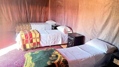 a bedroom with two beds and a table with a night stand at Tigmi Desert Camp in Merzouga
