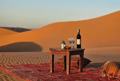 a table with a bottle of wine and glasses in the desert at Sandrock Luxury Camp in Merzouga