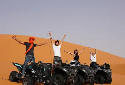three people standing on atvs in the desert at Sandrock Luxury Camp in Merzouga