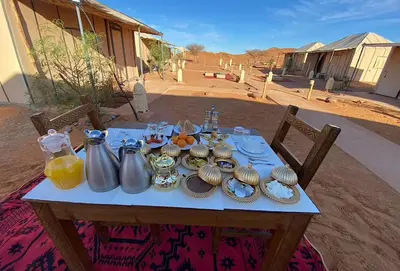 a table with utensils and plates of food on it at Sandrock Luxury Camp in Merzouga