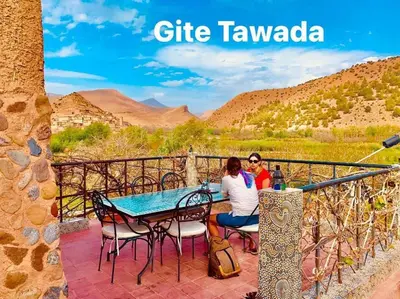two people sitting at a table on a patio with a view of the mountains at Hôtel Tawada in Azilal