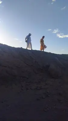 two people walking up a hill with backpacks at Merzouga camp in Merzouga