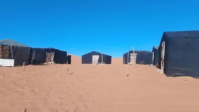 a row of black huts in the desert at Merzouga camp in Merzouga