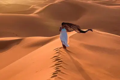 a woman walking on a sand dune in the desert at Merzouga Twilight Camp in Merzouga