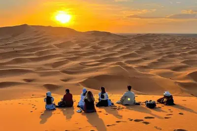 a group of people sitting in the desert watching the sunset at Merzouga Twilight Camp in Merzouga