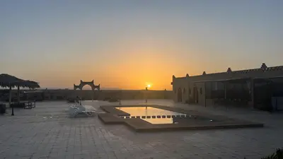 a sunset behind a building with a fountain in a courtyard at Hotel Berber Palace Merzouga in Merzouga