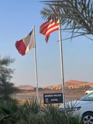 two flags on a beach with a car and a sign at Hotel Berber Palace Merzouga in Merzouga