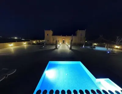 a swimming pool in front of a building at night at Hotel Berber Palace Merzouga in Merzouga