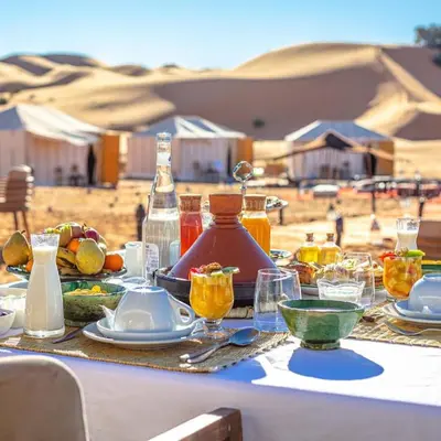 a table with food and drinks on it in the desert at Merzouga whisper camp in Merzouga