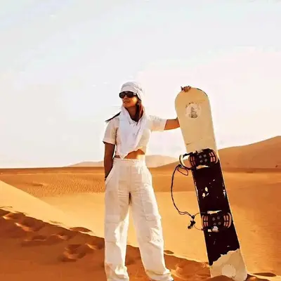 a woman standing in the desert holding a snowboard at Merzouga whisper camp in Merzouga