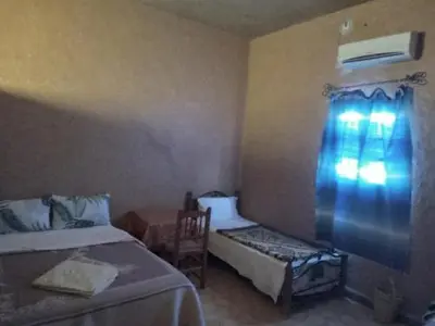a bedroom with two beds and a chair and a window at Gite Omar merzouga in Merzouga
