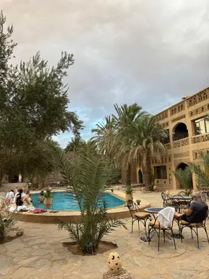 a pool with people sitting in chairs next to a building at Ksar merzouga luxury camp in Merzouga