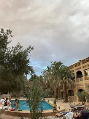 a courtyard with a swimming pool with palm trees and a building at Ksar merzouga luxury camp in Merzouga