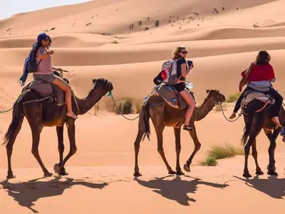 three women riding on camels in the desert at Maps of dreams camp in Merzouga