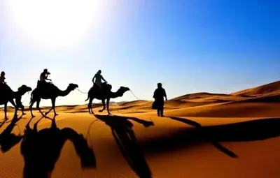 a group of people riding camels in the desert at Maps of dreams camp in Merzouga