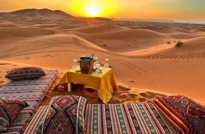a table in the middle of a desert with the sunset at Maps of dreams camp in Merzouga