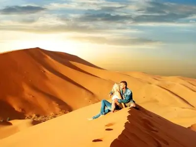 a man and woman sitting on top of a sand dune at Maps of dreams camp in Merzouga