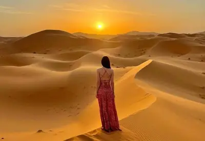 a woman standing in the desert watching the sunset at Sahara Moon Luxury Camp in Merzouga