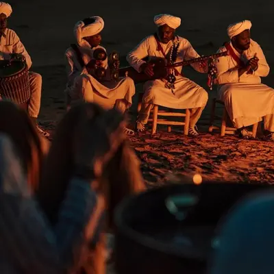 a group of men in white sitting around a fire at Sahara Moon Luxury Camp in Merzouga