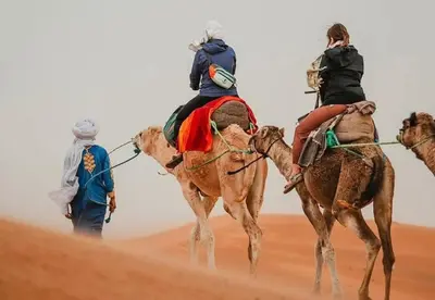 three people riding on camels in the desert at Sahara Moon Luxury Camp in Merzouga