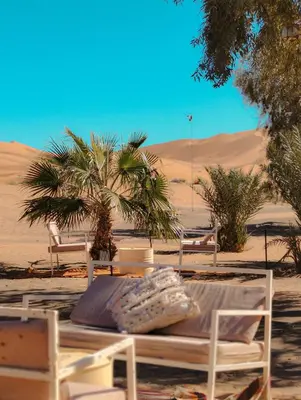 a table and chairs in the desert with palm trees at Merzouga Boho Camp in Merzouga