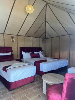 two beds in a tent with a table and chairs at Merzouga Sahara Nights Tents in Merzouga