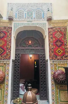 a room with colorful carpets on the wall and a room with a table at Riad Panoramik in Fès