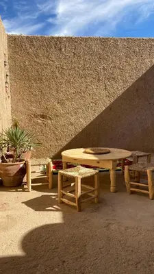 a picnic table and two chairs next to a wall at Merzouga Nomad House in Merzouga