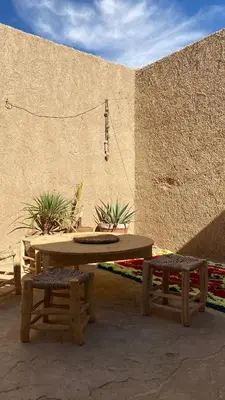 a picnic table and two benches in front of a wall at Merzouga Nomad House in Merzouga