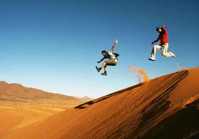 two people jumping off a sand dune in the desert at Sahara Relax Camps in Zagora
