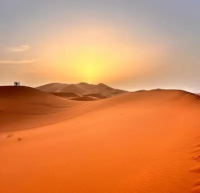 a group of people standing on top of sand dunes in the desert at Sahara desierto Camp in Merzouga