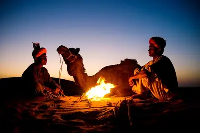 two men and a camel sitting around a fire at Merzouga Desert Dreams in Merzouga