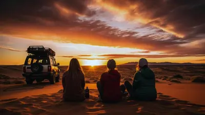 a group of people sitting in the desert watching the sunset at Merzouga Desert Dreams in Merzouga