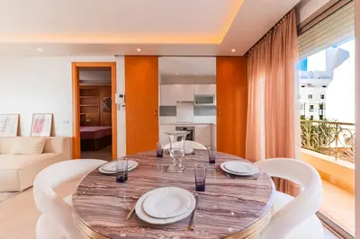a dining room with a wooden table and white chairs at Riva Molière Parking Elegance in Oulad Akkou