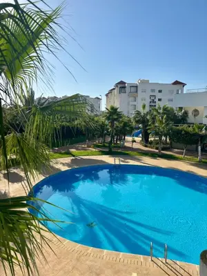 a large blue swimming pool with palm trees and buildings at Le cocon d'Asilah Mer et Confort in Oulad Akkou