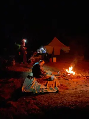 a man sitting next to a fire at night at Bivouac Desert Du Maroc in Mhamid