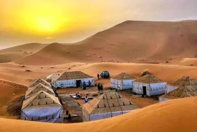 a group of tents in the desert with a sunset at kasbah estrella in Merzouga