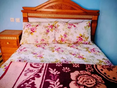 a bed with a wooden headboard and a bedspread with flowers at Auberge le calme restaurante in Bou Tharar