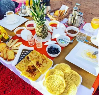 a table with breakfast foods and fruit on it at Itran luxury camp in Merzouga