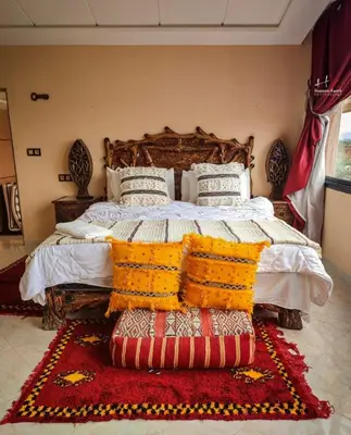 a bedroom with a large bed with a red rug at Tynass Ferme - Atlas Room Fes
