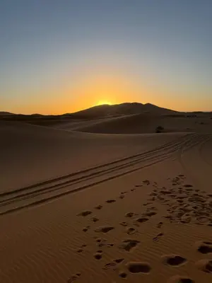 a sunset in the desert with footprints in the sand at Merzouga in Merzouga