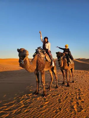 three people riding on the backs of camels in the desert at Merzouga delicioso Camp in Oulad Akkou