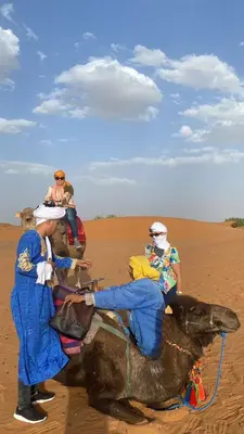 a group of people riding on the back of a camel in the desert at Merzouga delicioso Camp in Oulad Akkou