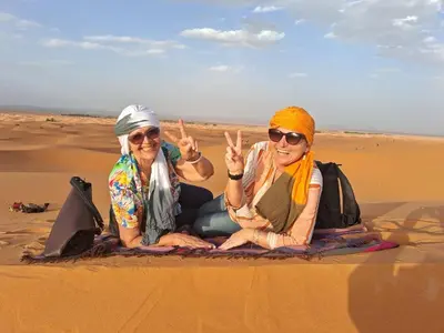 two women sitting in the sand in the desert at Merzouga delicioso Camp in Oulad Akkou