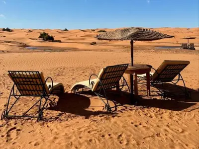 three chairs and a table with an umbrella in the desert at Merzouga Joy Camp in Hassilabied