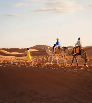 three people riding on camels in the desert at Golden dunes luxury camp in Merzouga